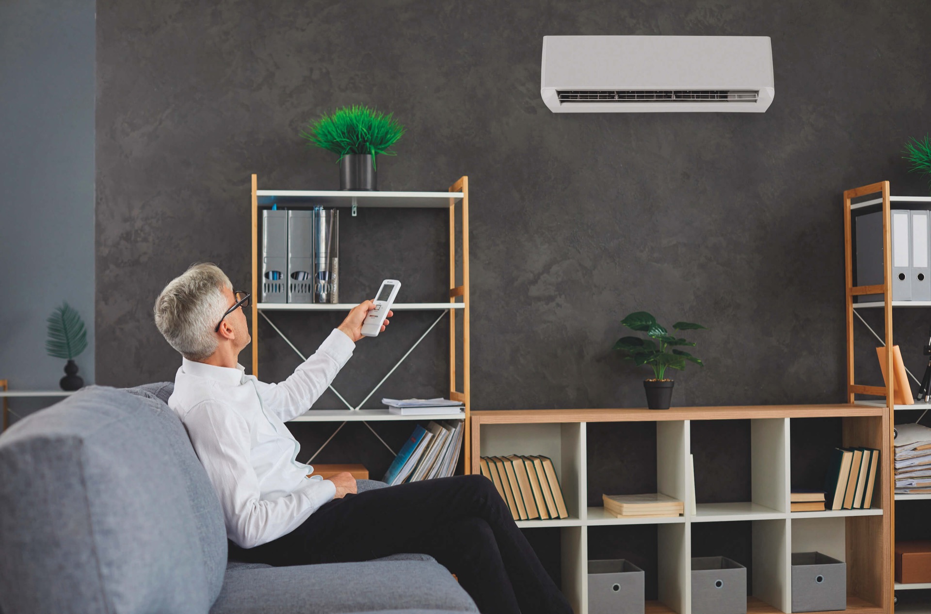 Klimaanlage im Wohnzimmer, ein Bewohner bedient die Fernbedienung